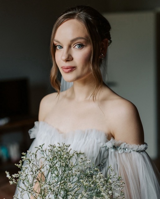 Bridal portrait featuring soft romantic makeup with nude lips, defined eyes, and a classic updo with loose strands, highlighting the natural beauty of the bride in a timeless style