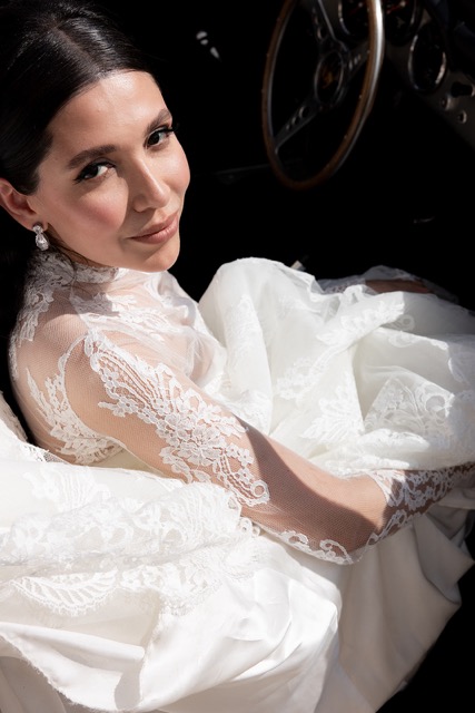 Elegant bride in a lace gown with classic bridal makeup, featuring flawless skin, subtle contouring, and defined lashes, with sleek center-parted hair, showcasing timeless bridal beauty.