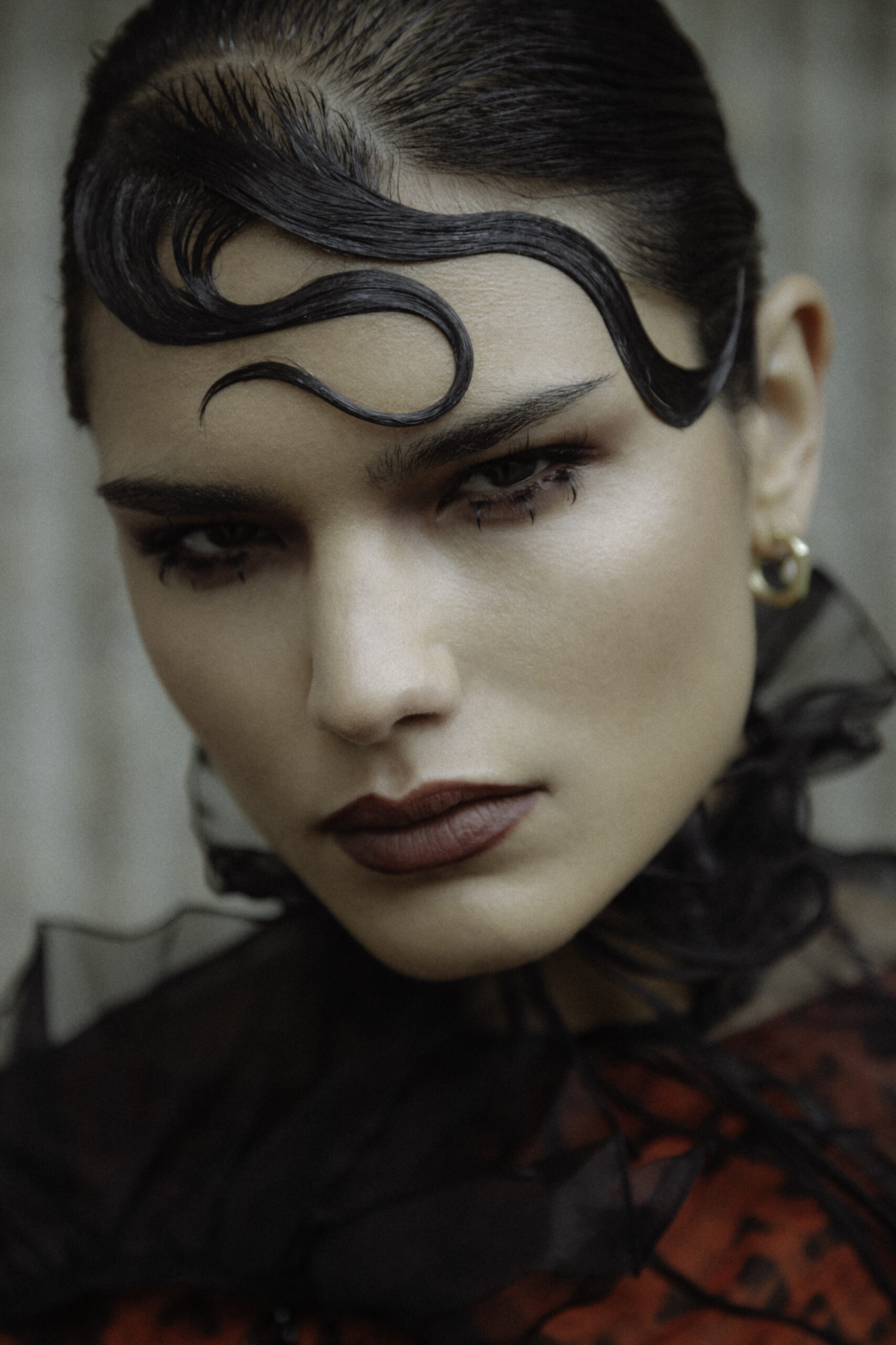 Model with avant-garde makeup featuring deep bordeaux lips, bold graphic eyeliner, and slicked-back hair with intricate finger waves, creating a dramatic and artistic high-fashion look