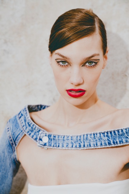 Model with bold red lips and graphic eyeliner, styled with sleek hair and wearing a denim top, creating a fierce editorial makeup look