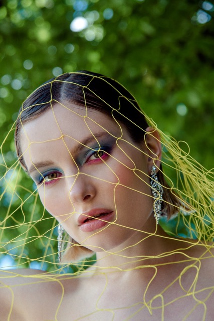 Model with bold colorful eyeshadow and a yellow modern veil, wearing crystal earrings for an avant-garde editorial look.